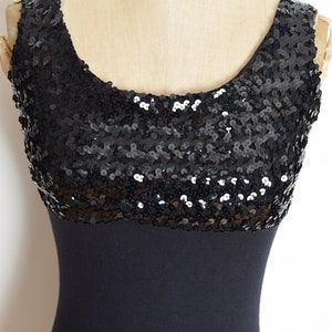 May include: A black sleeveless dress with a sequined top and a solid black bottom. The dress is on a mannequin.