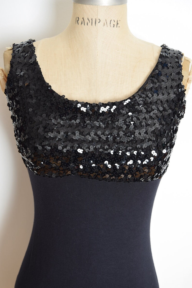 May include: A black sleeveless dress with a sequined top and a solid black bottom. The dress is on a mannequin.