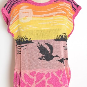 May include: A pink, yellow, orange, and black sleeveless knitted sweater with a sunset and bird design. The sweater has the word "Rampage" on the label.
