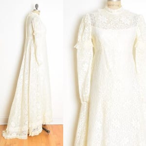 May include: A white lace wedding dress with long sleeves and a high neck. The dress has a fitted bodice and a flowing skirt.