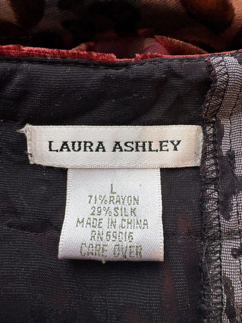 May include: Close-up of a clothing tag from Laura Ashley. The tag is white with black text, including the brand name, size, and fabric composition: 71% rayon, 29% silk. The tag also indicates the item was made in China.