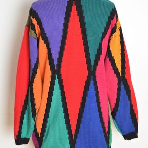 May include: A colorful, vintage sweater with a geometric diamond pattern. The sweater features a black neckline and trim, and a vibrant array of colors including red, purple, green, orange, and blue. The sweater is displayed on a mannequin.