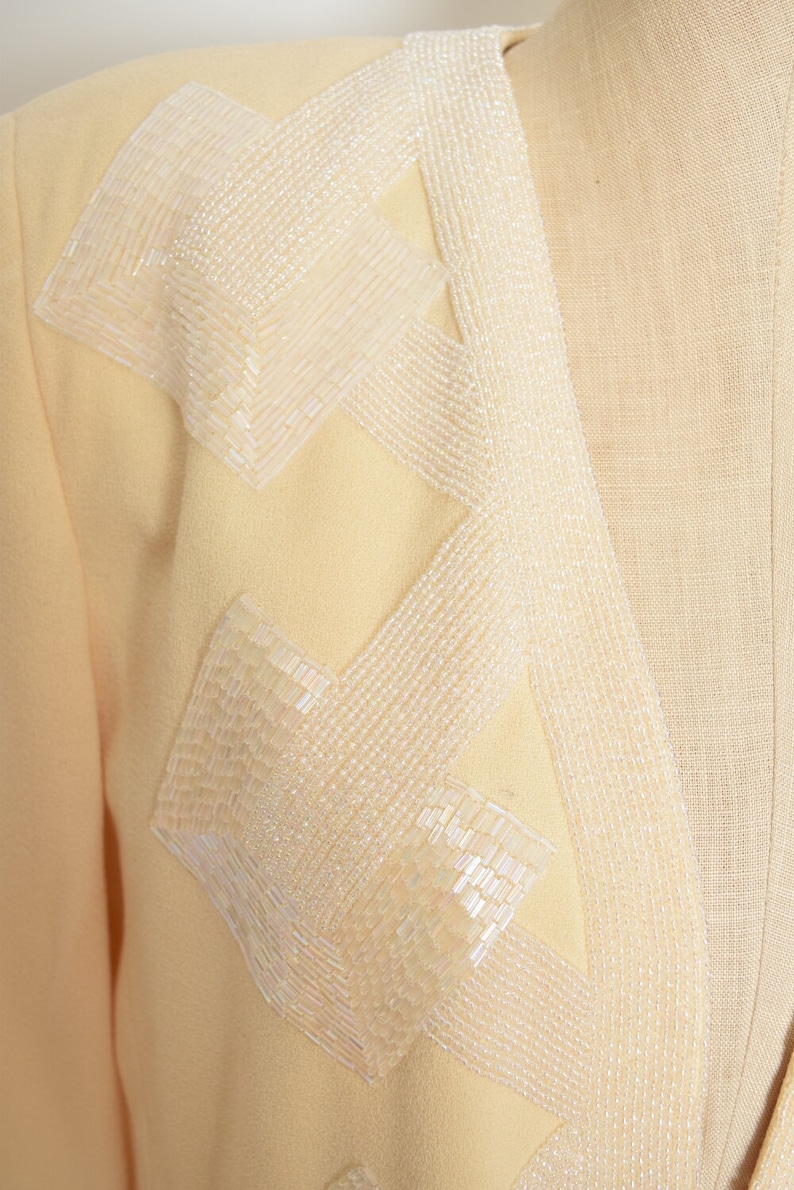 May include: A pale yellow blazer with a decorative design of white beads sewn in a geometric pattern.