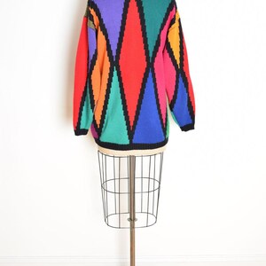 May include: A colorful sweater with a geometric diamond pattern in red, purple, green, blue, orange, and pink, outlined in black. The sweater is displayed on a wire dress form against a white background.