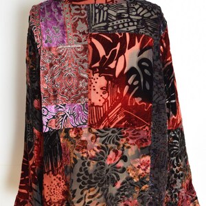 May include: A patchwork velvet top in shades of red, purple, and black. The long-sleeved garment features a variety of patterned fabrics, including floral and geometric designs. The top is displayed on a mannequin.