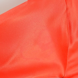 May include: A bright orange long-sleeved shirt with a black belt.