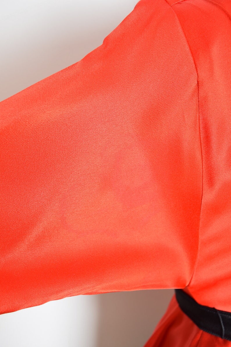May include: A bright orange long-sleeved shirt with a black belt.