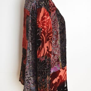 May include: A patchwork velvet jacket in shades of red, black, and purple. The jacket features a variety of floral and paisley patterns. The long-sleeved jacket has a V-neck and a loose fit.