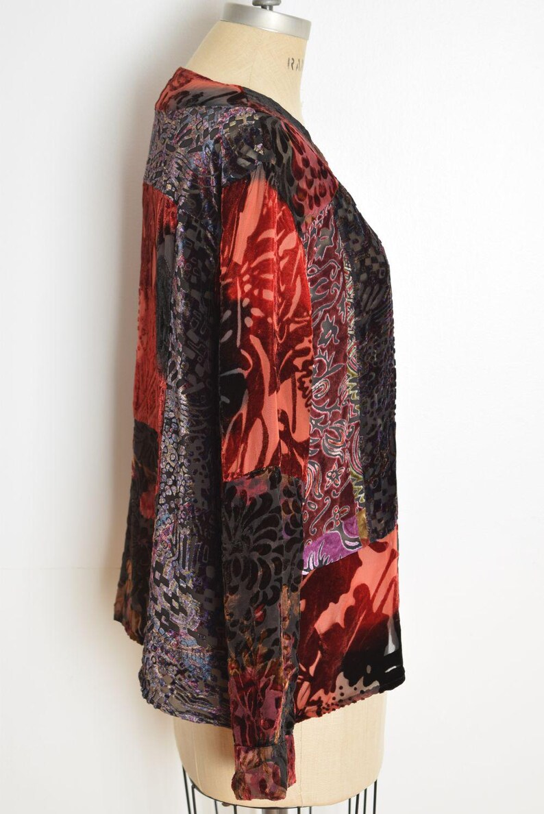May include: A patchwork velvet jacket in shades of red, black, and purple. The jacket features a variety of floral and paisley patterns. The long-sleeved jacket has a V-neck and a loose fit.
