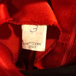 May include: Red satin fabric with a white tag that says "Size 5/6" and "Dry Clean Only".