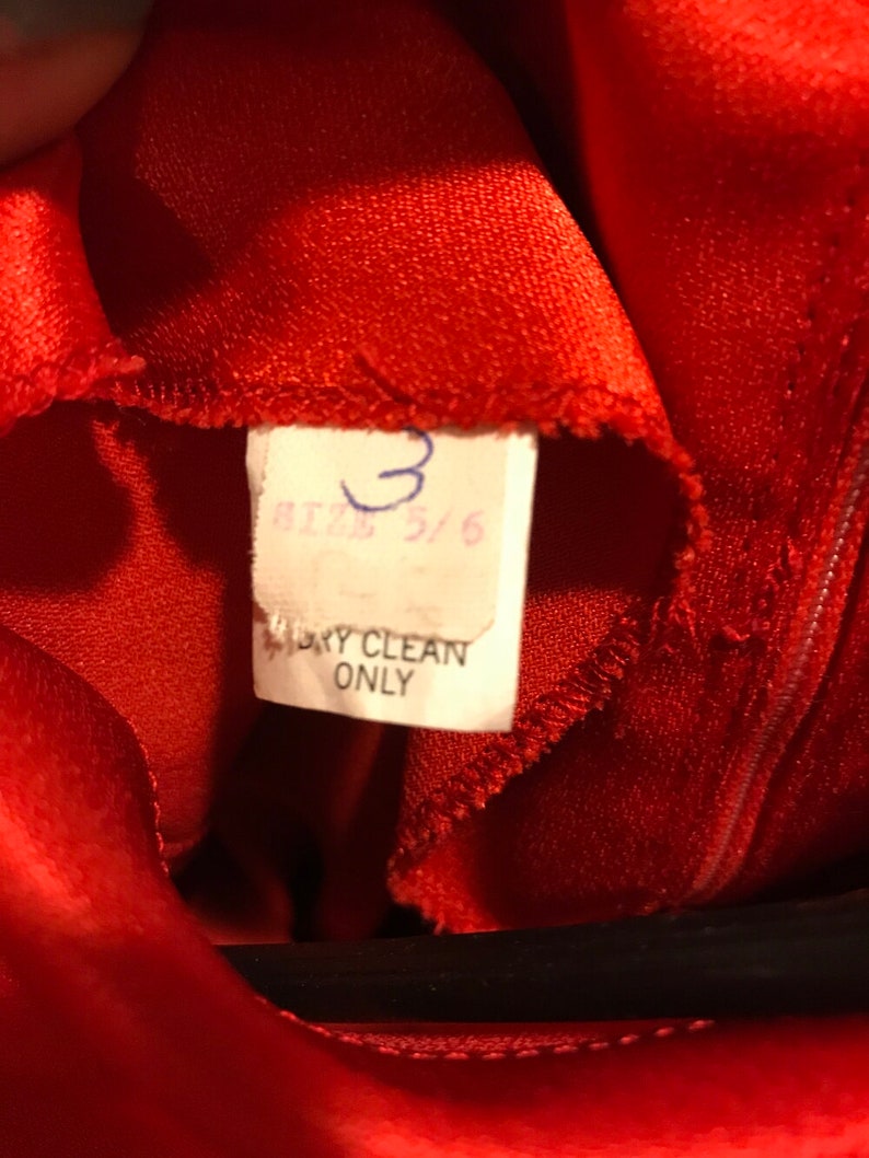 May include: Red satin fabric with a white tag that says "Size 5/6" and "Dry Clean Only".