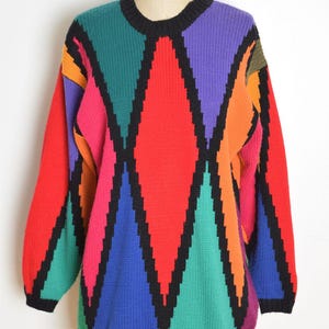 May include: A vintage, oversized sweater with a bold geometric pattern. The sweater features large diamond shapes in red, purple, green, blue, orange, and pink, outlined in black. The neckline and cuffs are black. The brand name "RAMPAGE" is visible on the mannequin.