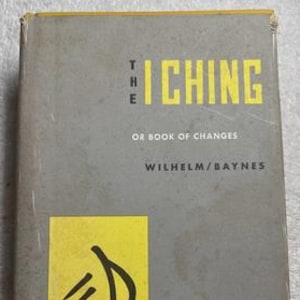 May include: A vintage copy of "The I Ching or Book of Changes" by Wilhelm/Baynes. The book has a gray cover with yellow lettering and a yellow square with a black symbol. Published by Princeton University Press.