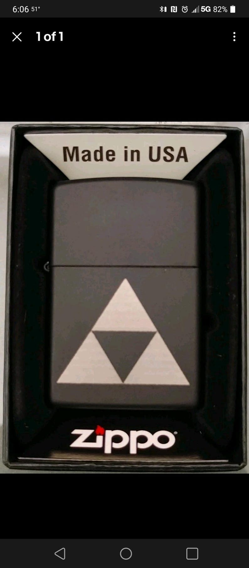 Puede incluir: Encendedor Zippo negro con un dise&ntilde;o de tri&aacute;ngulo blanco. El encendedor est&aacute; en una caja negra con "Made in USA" impreso en la parte superior. El logotipo de Zippo es visible en la parte inferior.