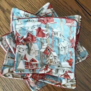 May include: Set of four blue and red quilted pot holders with a winter birdhouse pattern. The pot holders have a red trim and are made of a soft, quilted fabric.