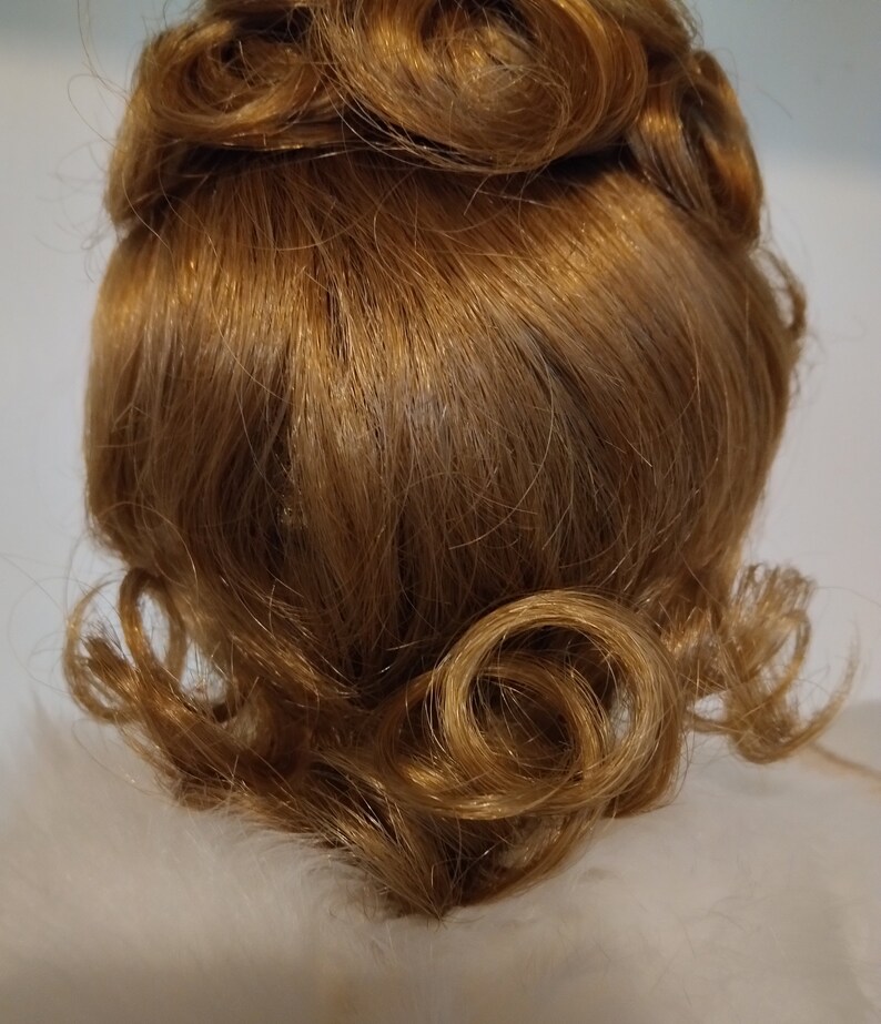 May include: A close-up of a brown wig styled in a vintage updo with curls. The wig is made of synthetic hair and has a natural-looking finish.