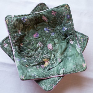 Può includere: Un copri ciotola trapuntato verde e rosa con un motivo floreale con farfalle e fiori. Il copri ciotola è realizzato in tessuto e ha un design trapuntato.