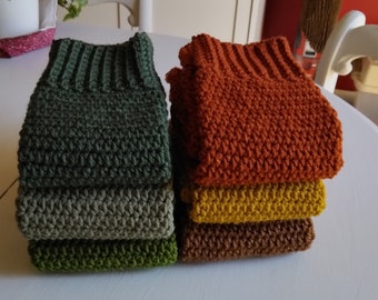 May include: A stack of five crocheted scarves in various shades of green, brown, and orange. The scarves are made with a textured stitch and are arranged in a neat pile.
