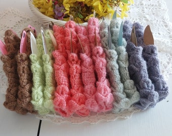 May include: A set of ten crocheted fingerless gloves in various colors, including brown, green, pink, blue, and gray. The gloves are arranged in a row, with the tips of the fingers pointing towards the viewer.