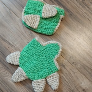 May include: A crocheted baby diaper cover and a matching crocheted turtle toy. The diaper cover is green with a white trim and the turtle is green with a white belly and feet.