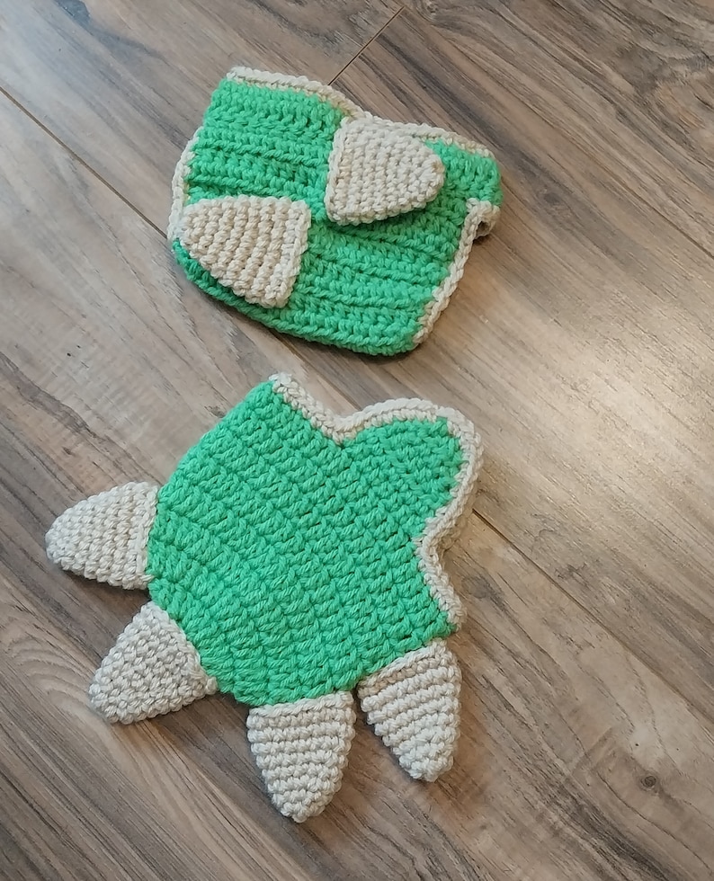 May include: A crocheted baby diaper cover and a matching crocheted turtle toy. The diaper cover is green with a white trim and the turtle is green with a white belly and feet.