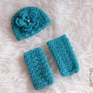 May include: A set of teal crocheted baby accessories, including a hat with a flower design and two matching wrist warmers.