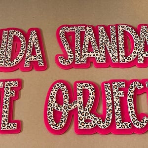 May include: Four hot pink, die-cut words: AGENDA, STANDARD, DATE, and OBJECTIVE. The letters are filled with a leopard print pattern. The words are arranged on a neutral background.
