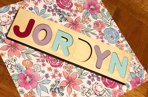 A chunky wooden name puzzle cut to the child's actual name — a tactile, screen-free baby gift that doubles as wall decor and a learning toy.
