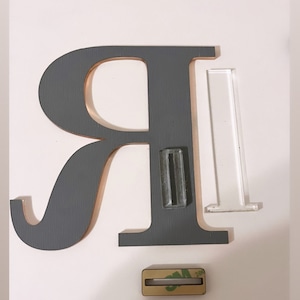 May include: A gray wooden letter R with a clear acrylic stand and a small piece of adhesive tape.