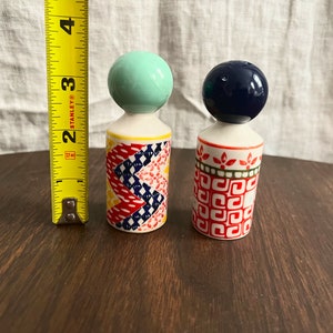May include: A pair of ceramic salt and pepper shakers. One shaker has a mint green ball top and a colorful geometric pattern. The other has a navy blue ball top and a red and white pattern. Each shaker is approximately 3 inches tall.