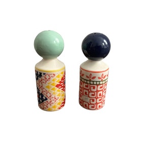 May include: A pair of ceramic salt and pepper shakers. One shaker has a light green ball-shaped top and a body decorated with a colorful geometric pattern. The other shaker has a dark blue ball-shaped top and a body with a red and green pattern.