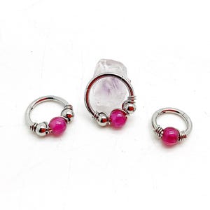 Peut inclure: Trois boucles d'oreilles créoles articulées argentées avec des perles roses. Les boucles d'oreilles sont disposées sur une surface blanche. Les perles sont d'un rose vif et les boucles d'oreilles sont de tailles différentes.
