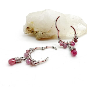 May include: Two silver-toned hinged hoop earrings featuring wire-wrapped faceted pink gemstone beads. Each hoop is adorned with multiple small pink stones and a single larger dangling pink bead, secured with thin silver wire coils.