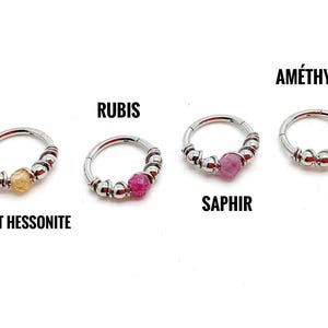 Peut inclure: Quatre anneaux de nez argentés, chacun avec une pierre précieuse différente : un grenat jaune-orangé, un rubis rose, un saphir rose et une améthyste violet clair. Les pierres précieuses sont au centre des anneaux.