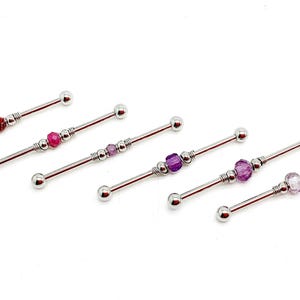 May include: Industrial barbell piercings with decorative beads in various colors, including red, pink, and purple. The jewelry is made of silver-colored metal and features a ball on each end.