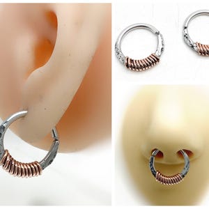 May include: A circular hoop ring featuring a textured silver-toned metal band accented with a section of coiled copper-colored wire. The design includes a hinged closure mechanism, shown inserted into a simulated earlobe and a simulated nasal septum.