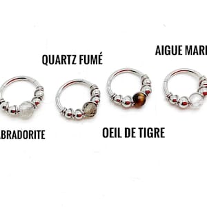 Peut inclure: Quatre boucles d'oreilles créoles argentées avec des pierres précieuses. Chaque boucle d'oreille présente une pierre différente : labradorite, quartz fumé, oeil de tigre et aigue-marine. Les noms des pierres sont imprimés.