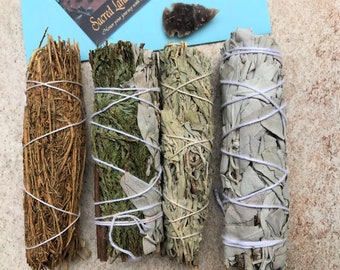 May include: Four bundles of dried herbs, tied with white string. The bundles range in colour from light brown to green and grey. A small, grey arrowhead and a blue card with text are also present.