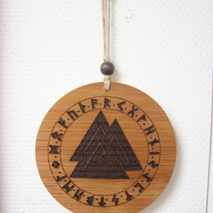 May include: A round wooden ornament with a dark brown wood-burned design of a Vegvisir symbol surrounded by runes. The ornament is hanging from a string with a brown bead.
