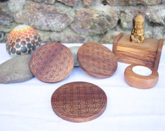May include: Four wooden coasters with a flower of life design, a small wooden box with a Buddha statue on top, and a wooden candle holder.
