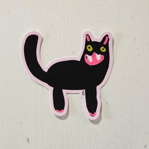 May include: A black cat sticker with pink outlines and yellow eyes. The cat has a large pink mouth with white teeth.