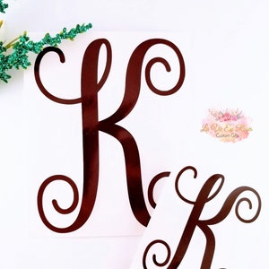 May include: Two brown vinyl decals of the letter K in a cursive font. The decals are on a white background.