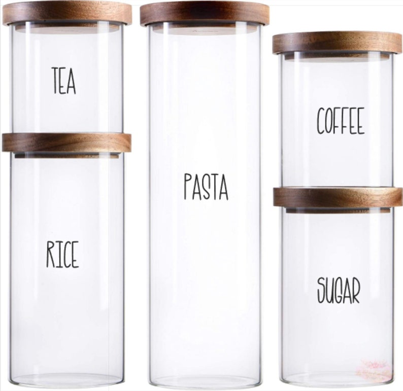 May include: Three glass canisters with wooden lids and labels. The canisters are labeled "TEA", "RICE", "PASTA", "COFFEE", and "SUGAR".