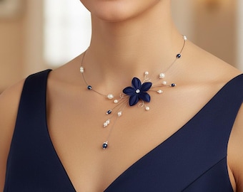 Könnte beinhalten: Eine marineblaue Blumenkette mit Perlen und dunkelblauen Perlenakzenten. Der Blumenanhänger hat einen zentralen Kristall. Die Halskette wird über einem marineblauen Kleid getragen.