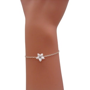 Peut inclure: Un bracelet délicat en chaîne argentée avec un charme de fleur blanche. La fleur a un petit strass au centre.