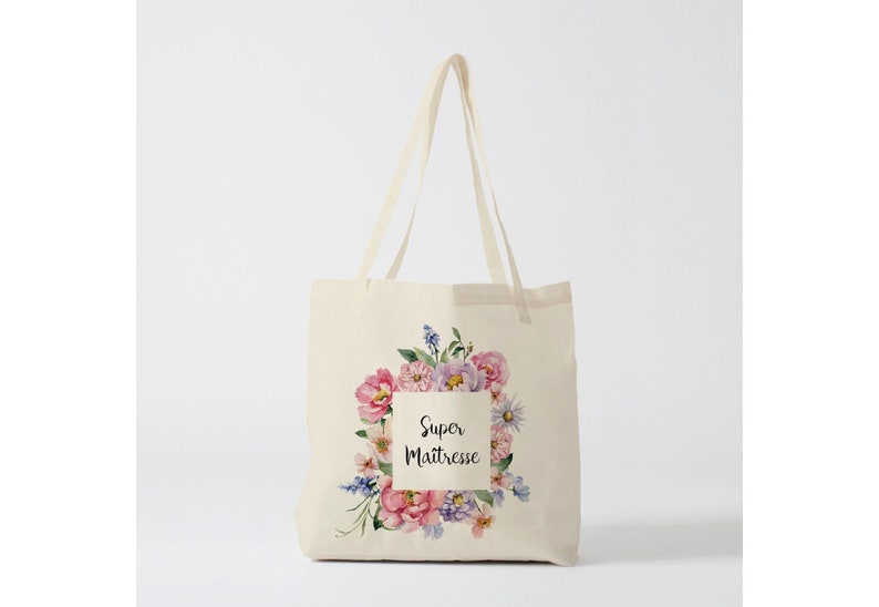 Puede incluir: Bolso tote color crema con un dise&ntilde;o floral y el texto "Super Ma&icirc;tresse". El arreglo floral incluye flores rosas, moradas y azules. El bolso tiene dos asas largas.