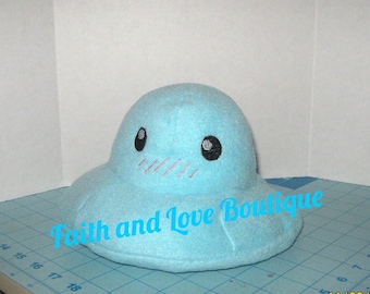 May include: A light blue plush toy shaped like a flying saucer with black eyes and a pink mouth. The toy has the text "Faith and Love Boutique" embroidered on the bottom.