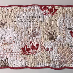 May include: A quilted placemat with a white background and a red border. The placemat features a vintage Parisian design with images of roosters and the text "VILLE DE PARIS 170. Rue Montmartre, 170".