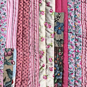 Pode incluir: Um tecido acolchoado com tiras verticais de vários padrões, incluindo riscas cor-de-rosa e brancas, pontos cor-de-rosa, tecido creme com pequenas rosas e estampados florais em tons de azul, verde e rosa, unidos por costuras retas.