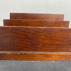 May include: A wooden desk organizer with three tiered compartments. The organizer is made of dark brown wood with a natural grain. The front of the organizer has a beveled edge. The item is designed to hold letters and documents.